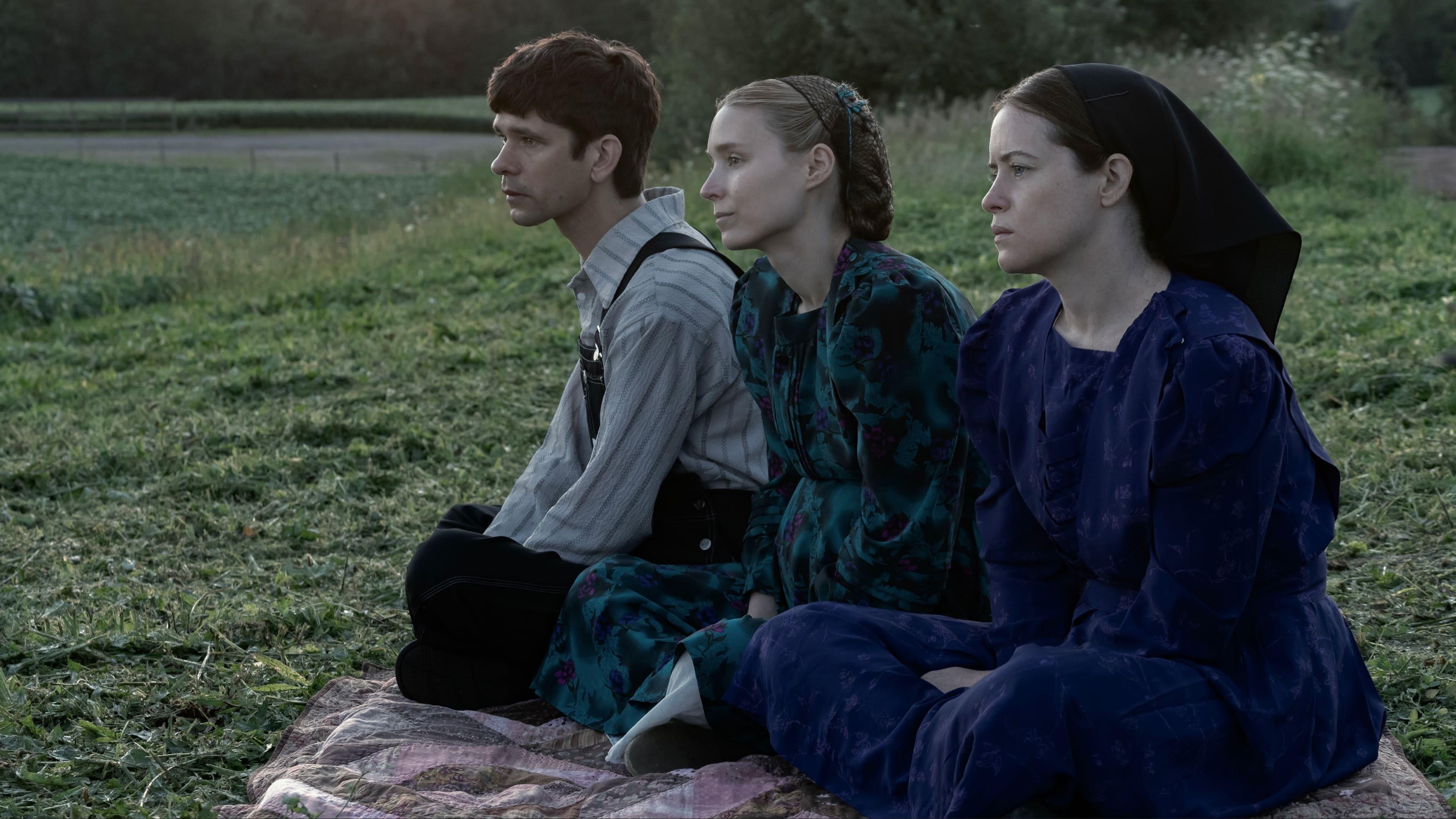 On a grassy plain sits a young man and two young women in period attire, staring blankly into the distance.